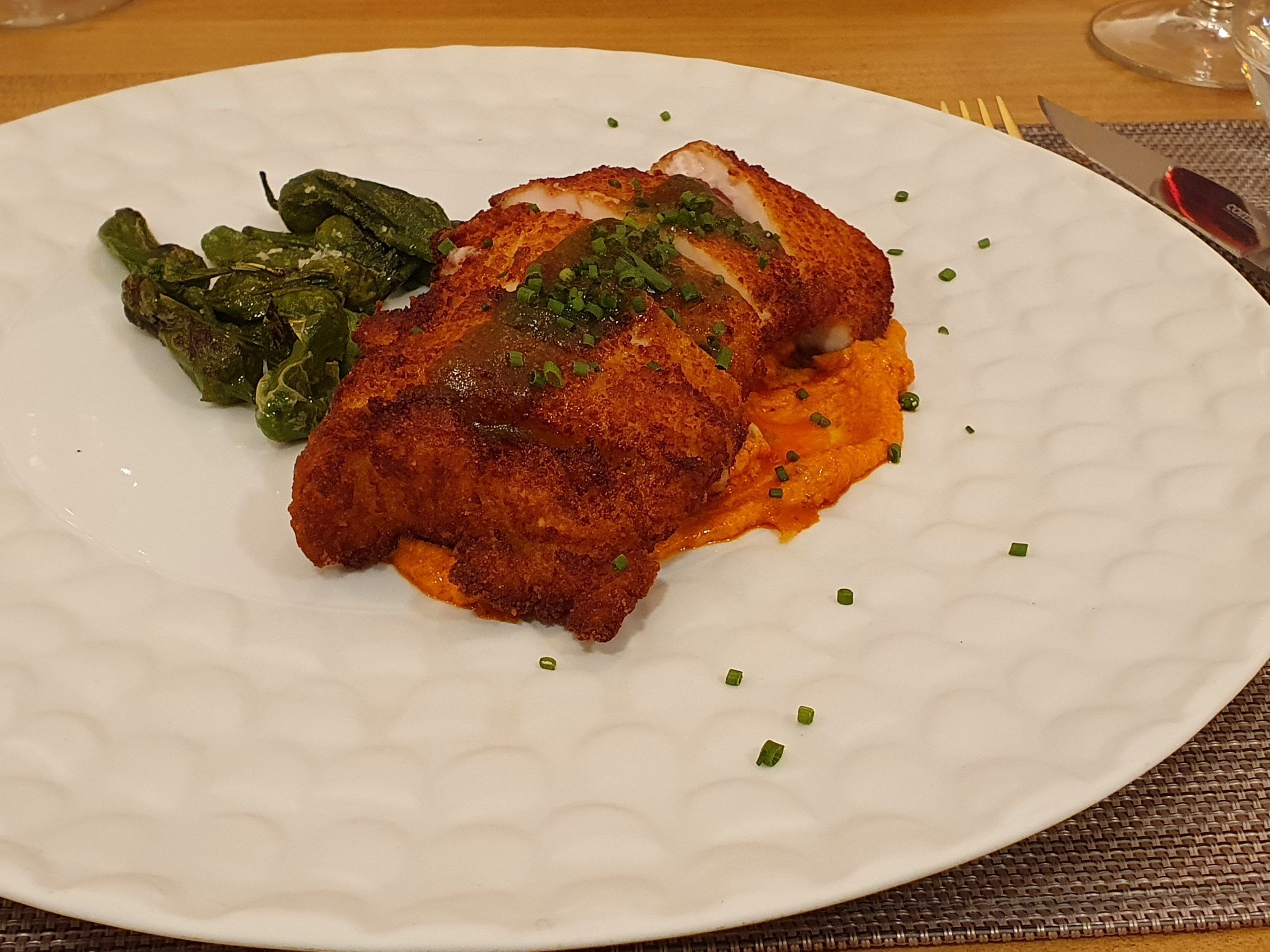 Cachopo de pollo de corral, relleno de jamón y queso sobre pesto rojo calabrese y pimiento de padrón